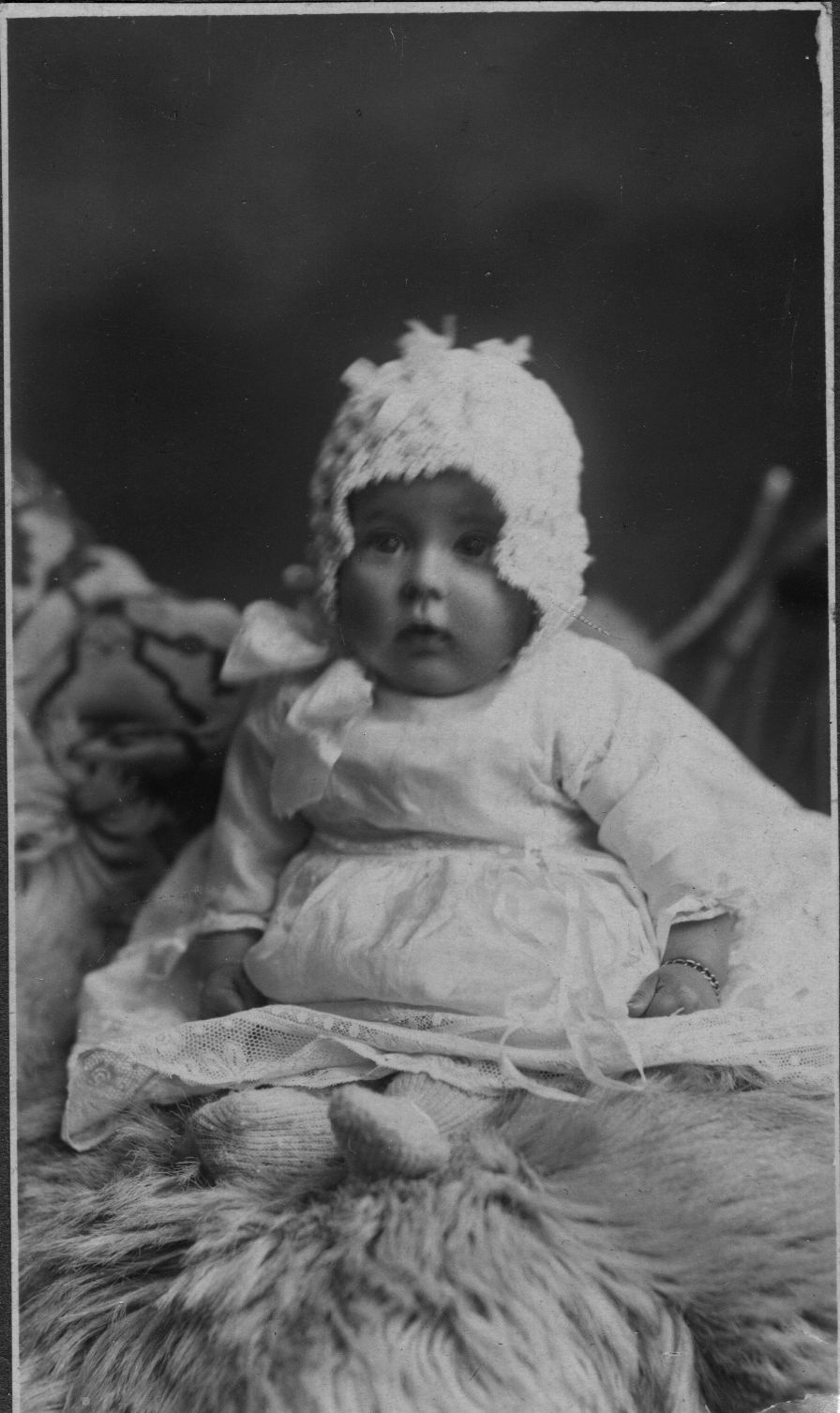 Dorothy as a baby dressed in a lacy baby dress, knitted bootees and a matching baby bonnet typical if the early 20th Century